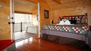 Ein Schlafzimmer einer Holzhütte mit einem Bett, einer Tür, die auf einen Balkon führt, und einem Schild mit der Aufschrift 'Welcome to the Mountain'.
