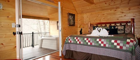 A wooden cabin bedroom with a bed, a door leading to a balcony, and a sign reading "Welcome to the Mountain".