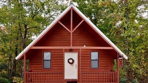 Eine kleine, eingeschossige Holzhütte mit einer weißen Tür, zwei Fenstern und einer Veranda.