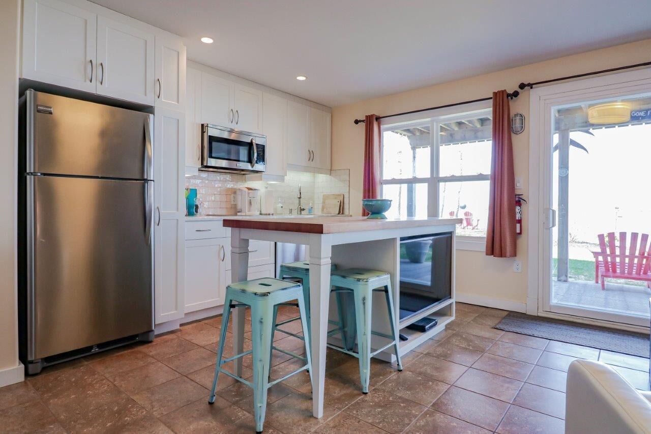 A kitchen with white cabinets, a stainless steel refrigerator, a microwave, and a window with a curtain.