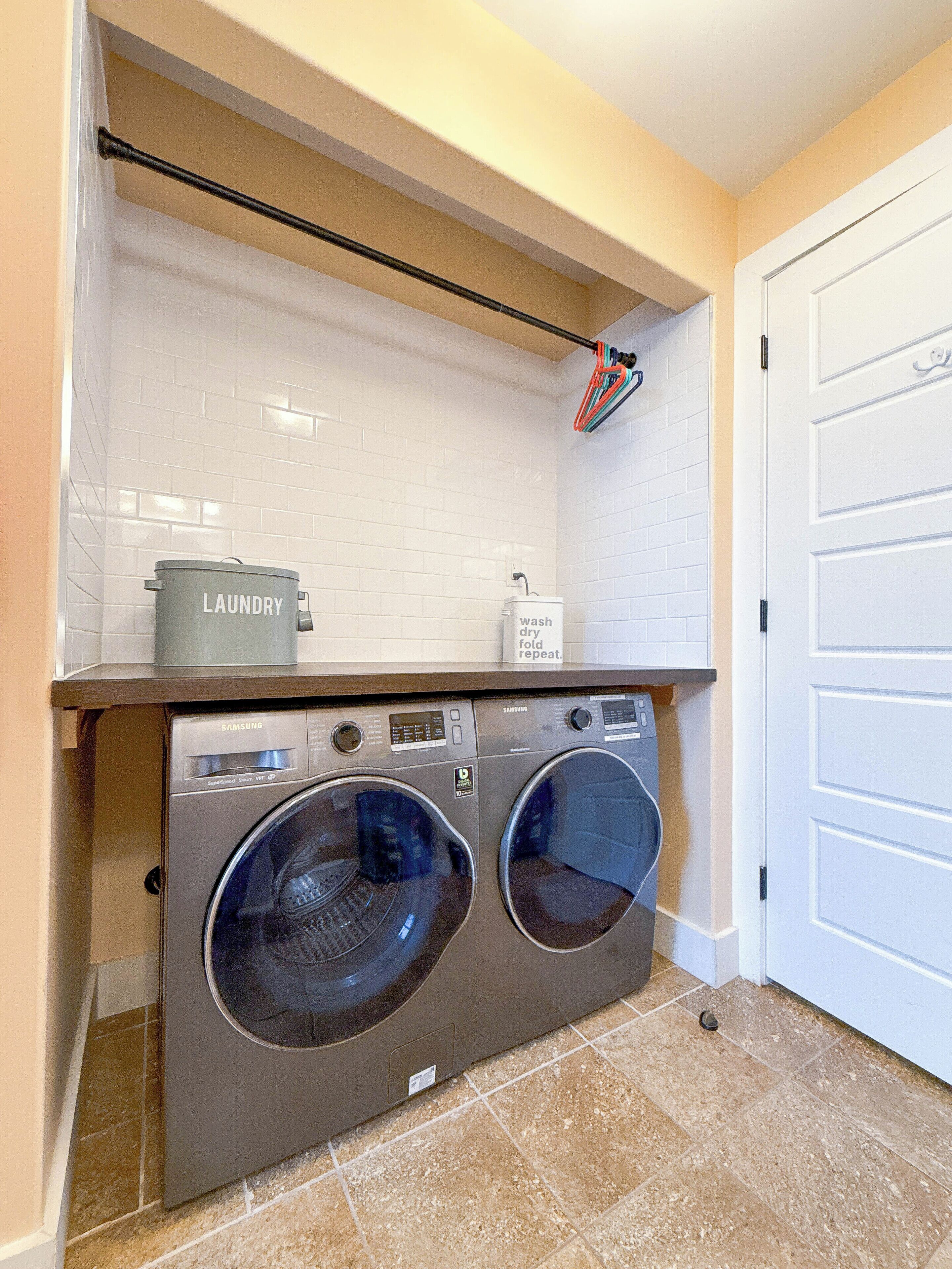 A laundry area with two front-loading washing machines, a drying rack, and a laundry basket.