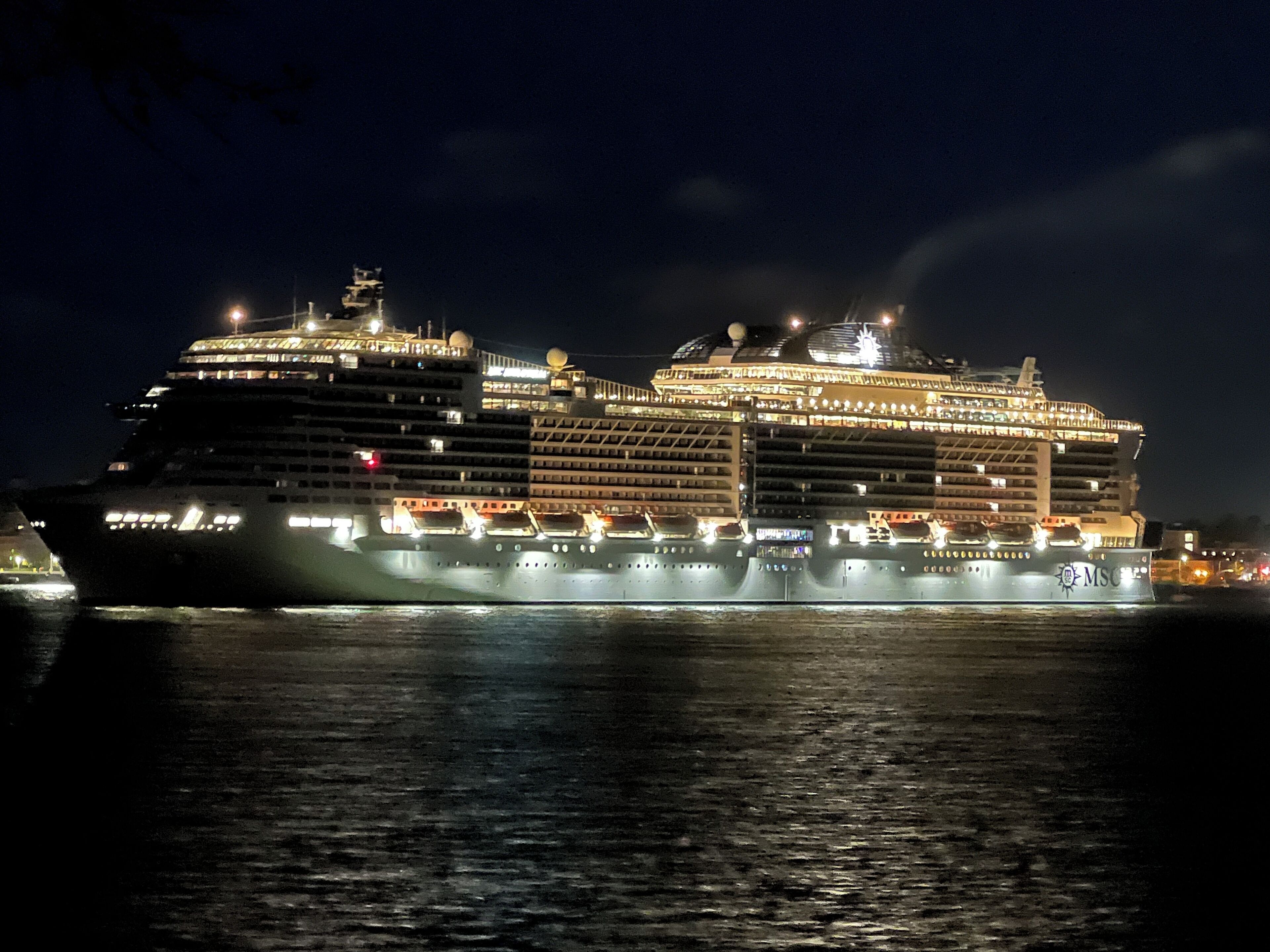 A large cruise ship with multiple decks and illuminated windows, docked at night.