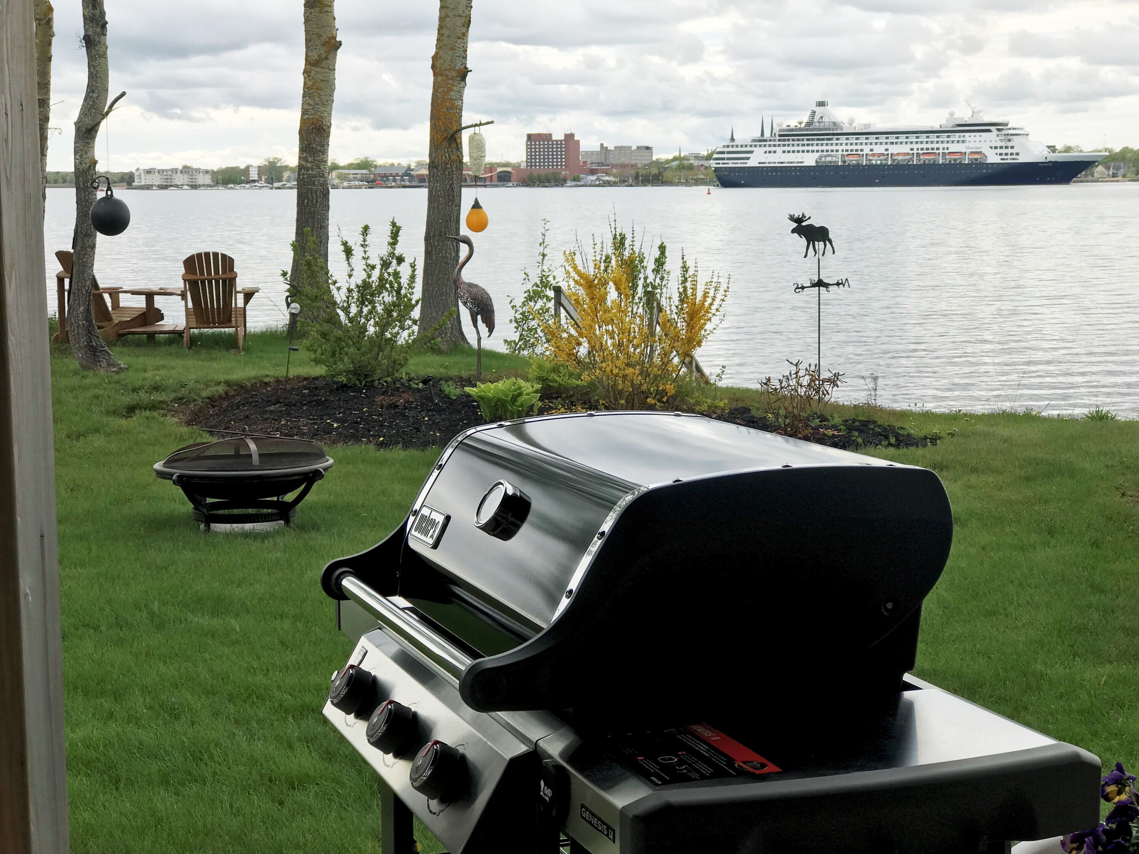 A backyard with a grill, outdoor furniture, and a view of a cruise ship on the water.