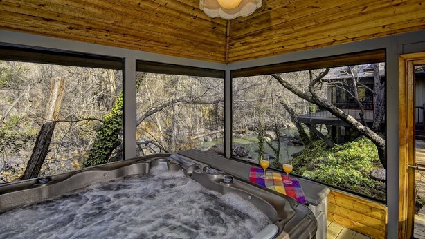 A hot tub with a wooden ceiling and large windows overlooking a natural landscape.