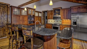 A rustic kitchen with wooden cabinets, a stainless steel refrigerator, and a bar area with stools.