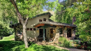 A stone house with a porch, surrounded by lush greenery.