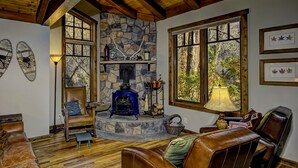 A cozy living room with a stone fireplace, leather furniture, and large windows offering a view of the outdoors.