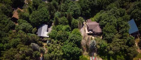 Vista aerea di una zona residenziale con una casa circondata da alberi fitti, un molo e diverse imbarcazioni.
