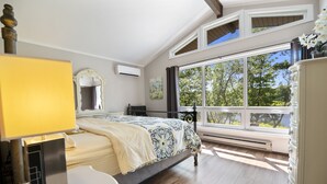 A bedroom with a bed, a desk, a dresser, a mirror, and a large window with a view of trees. - Inn Kognito 1 Lakefront, hot tub fire pit Kalahari 2nd house next door available (Emerald Lake)