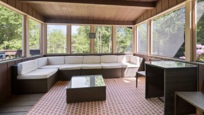 A covered outdoor seating area with a sectional sofa, a glass-top table, and wicker chairs. - Inn Kognito 1 Lakefront, hot tub fire pit Kalahari 2nd house next door available (Emerald Lake)