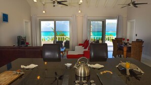 A modern hotel room with a dining area, a kitchen, and a balcony with a view of the ocean.