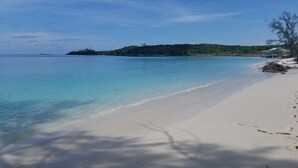 A beach with clear turquoise water, white sand, and a small island with greenery in the background.