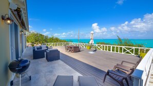 A deck with outdoor furniture, a grill, and a view of the ocean.