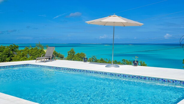 A clear blue pool with a tiled edge, a lounge chair, and an umbrella.