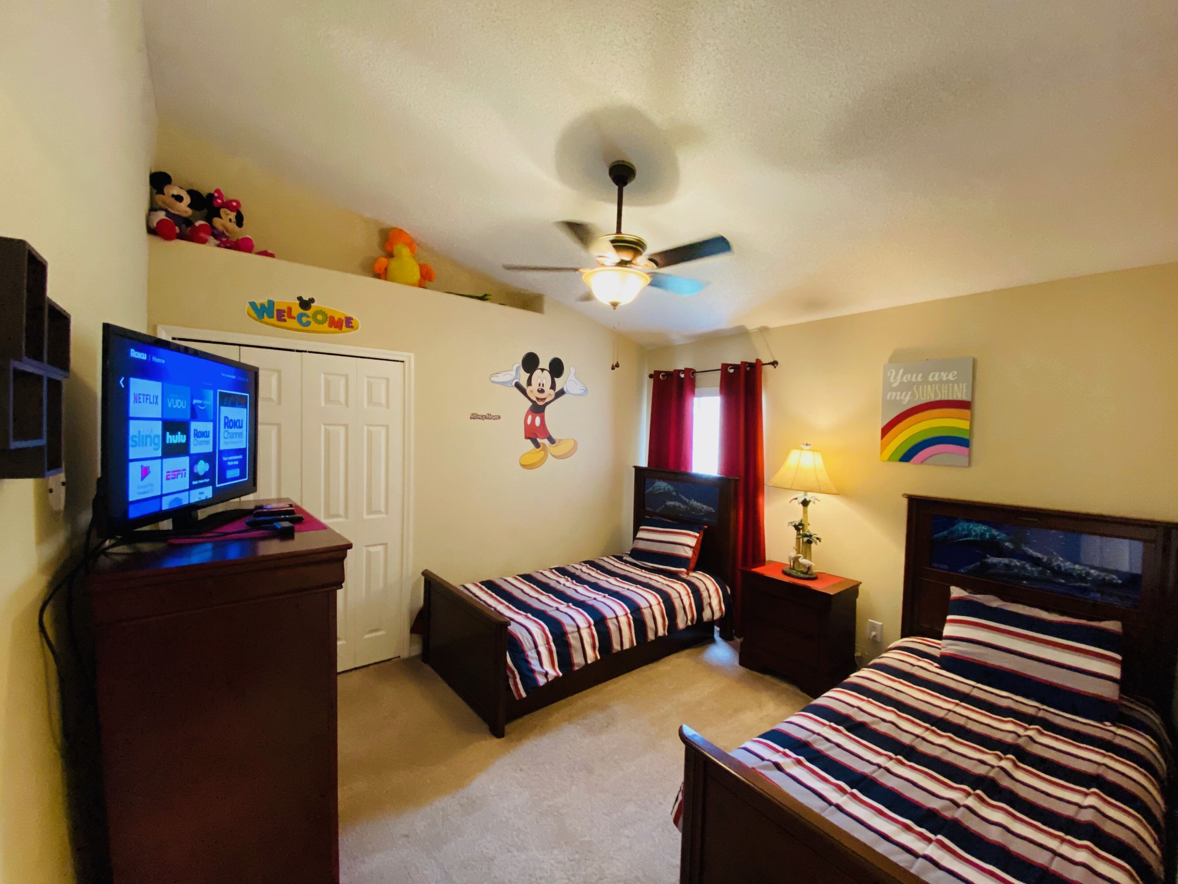 Ein Schlafzimmer mit zwei Betten, einem Deckenventilator, einem Fernseher und einer Wand mit Zeichentrickfiguren.