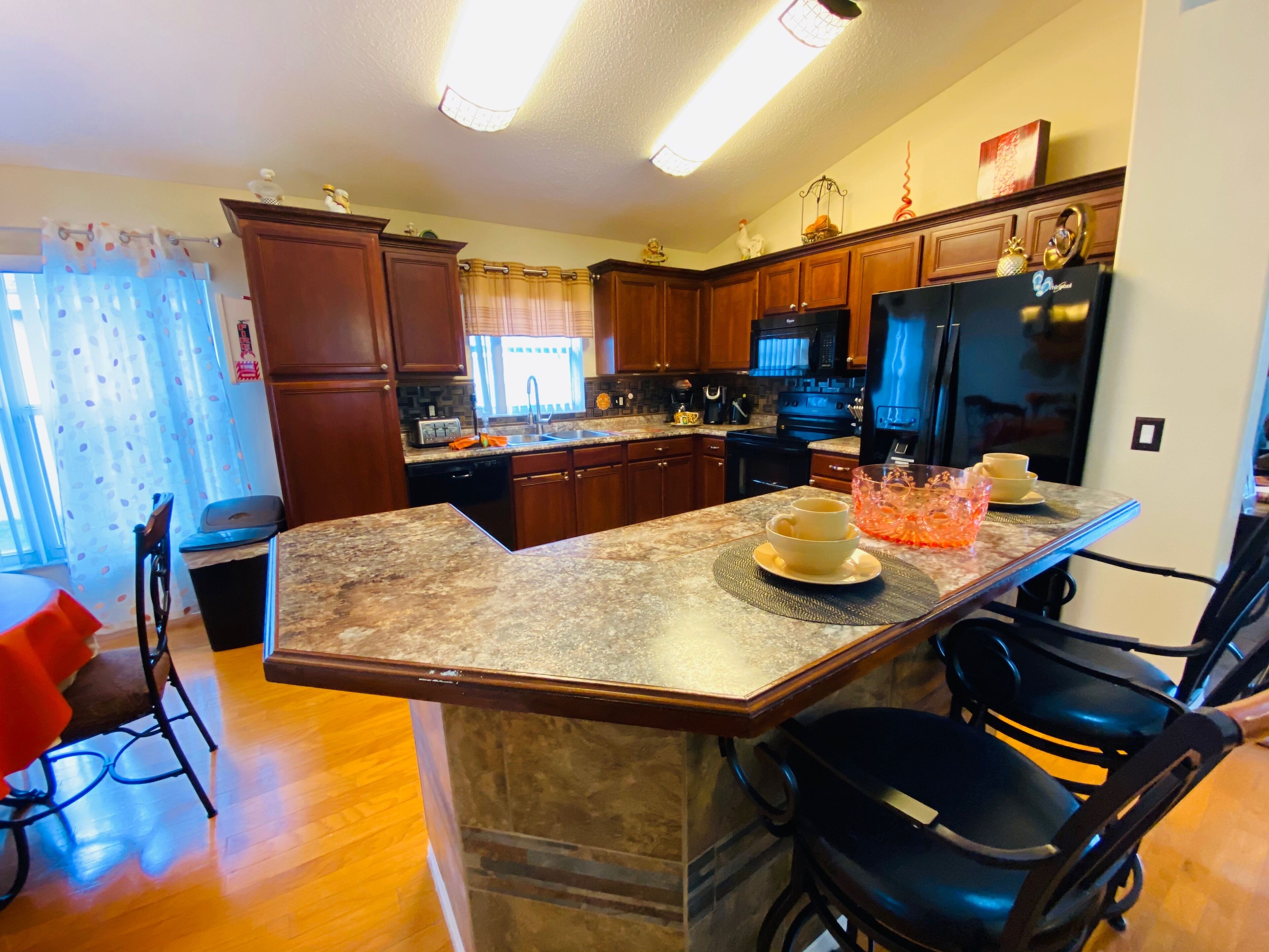A kitchen with wooden cabinets, granite countertops, a black refrigerator, and a dining area with a chair and a table.