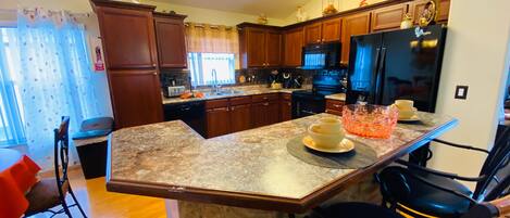 A kitchen with wooden cabinets, granite countertops, a black refrigerator, and a dining area with a chair and a table.