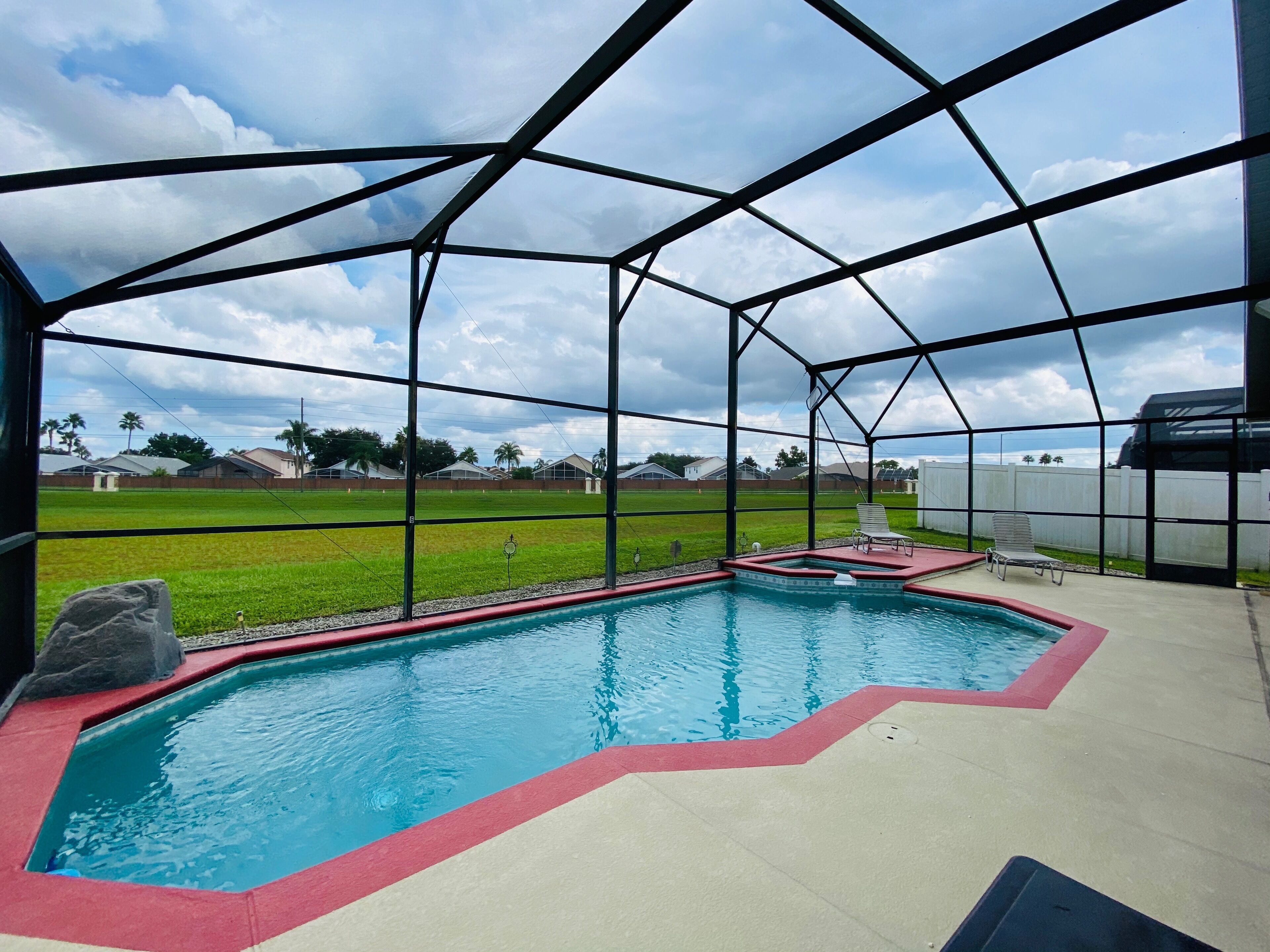 A covered outdoor swimming pool with a view of a grassy field and houses in the background.