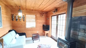 A wooden cabin interior with a sofa, television, fireplace, and wall-mounted animal horns. - The Huntsman Cabin (Warburton)