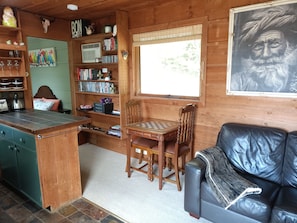 A cozy cabin interior with a wooden dining table, a leather couch, and a bookshelf filled with books and decorative items. - The Huntsman Cabin (Warburton)