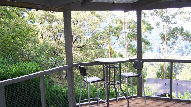 A covered outdoor area with a table and chairs, surrounded by a wooden deck and a metal railing. - The Huntsman Cabin (Warburton)