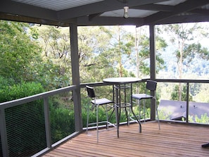 A covered outdoor area with a table and chairs, surrounded by a wooden deck and a metal railing.