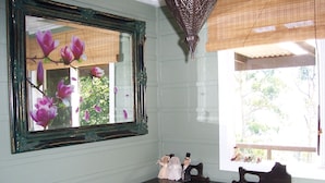 A room with a large mirror reflecting flowers, a dark wooden dresser, and a window with blinds. - The Huntsman Cabin (Warburton)