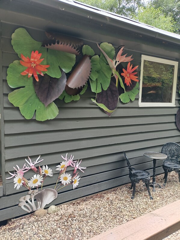 A building with a decorative wall featuring large leaves and flowers, a small table with chairs, and a window.