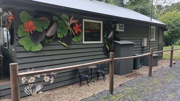 A rustic cabin with a metal roof, a wooden deck, and decorative foliage.