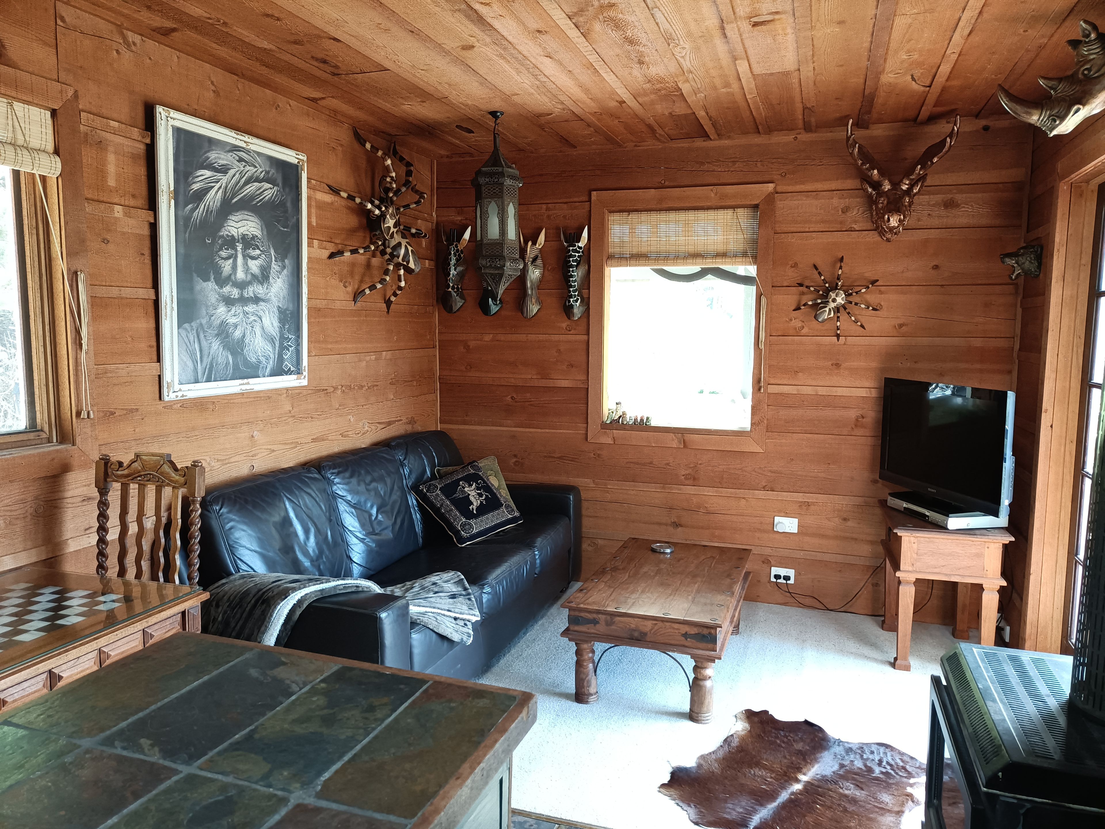 A wooden cabin interior with a leather sofa, a television, a chessboard, and various wall decorations.