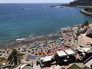 Une plage avec des parasols, des gens et des bateaux.