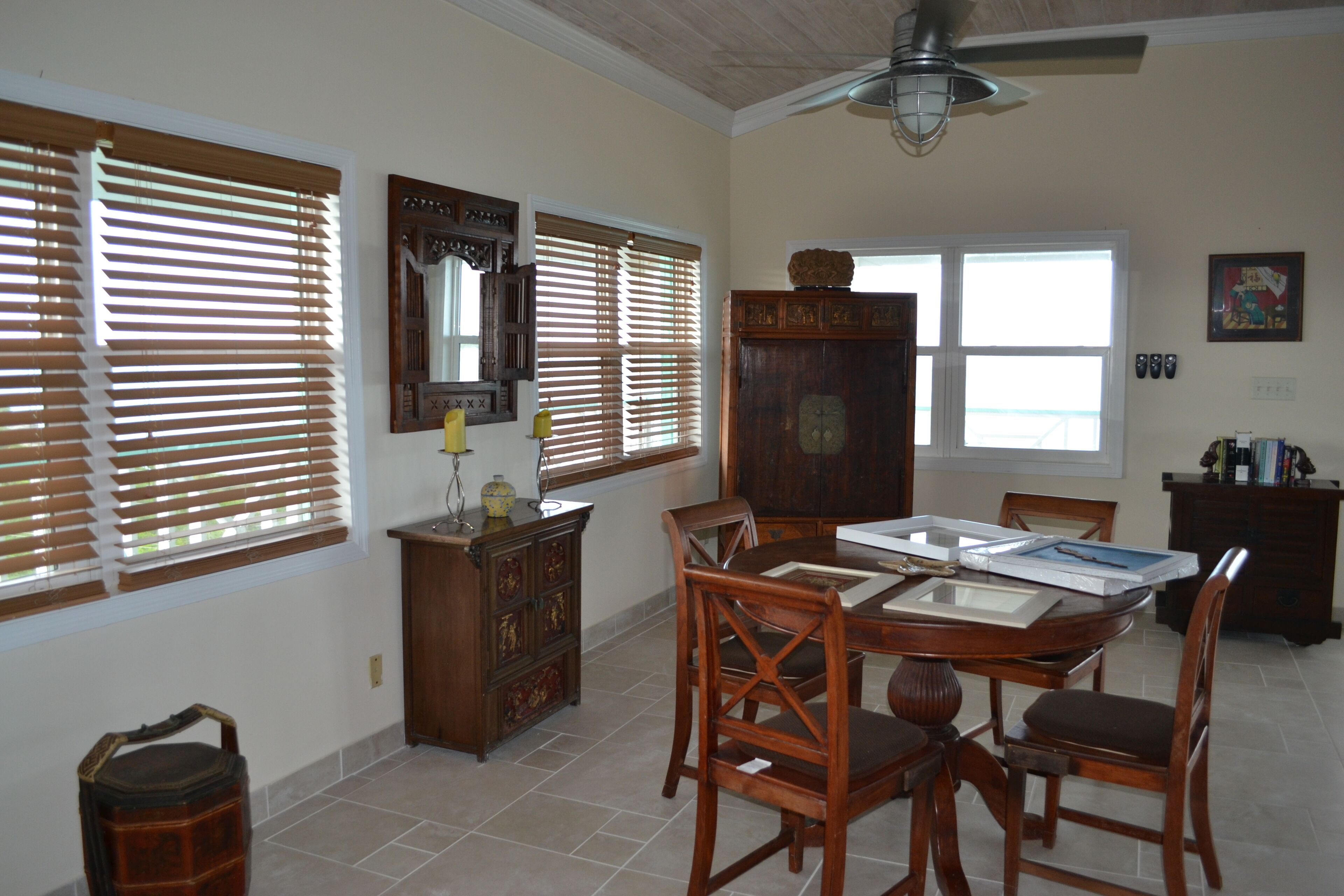 A dining area with a wooden table and chairs, a ceiling fan, and a large window with blinds.