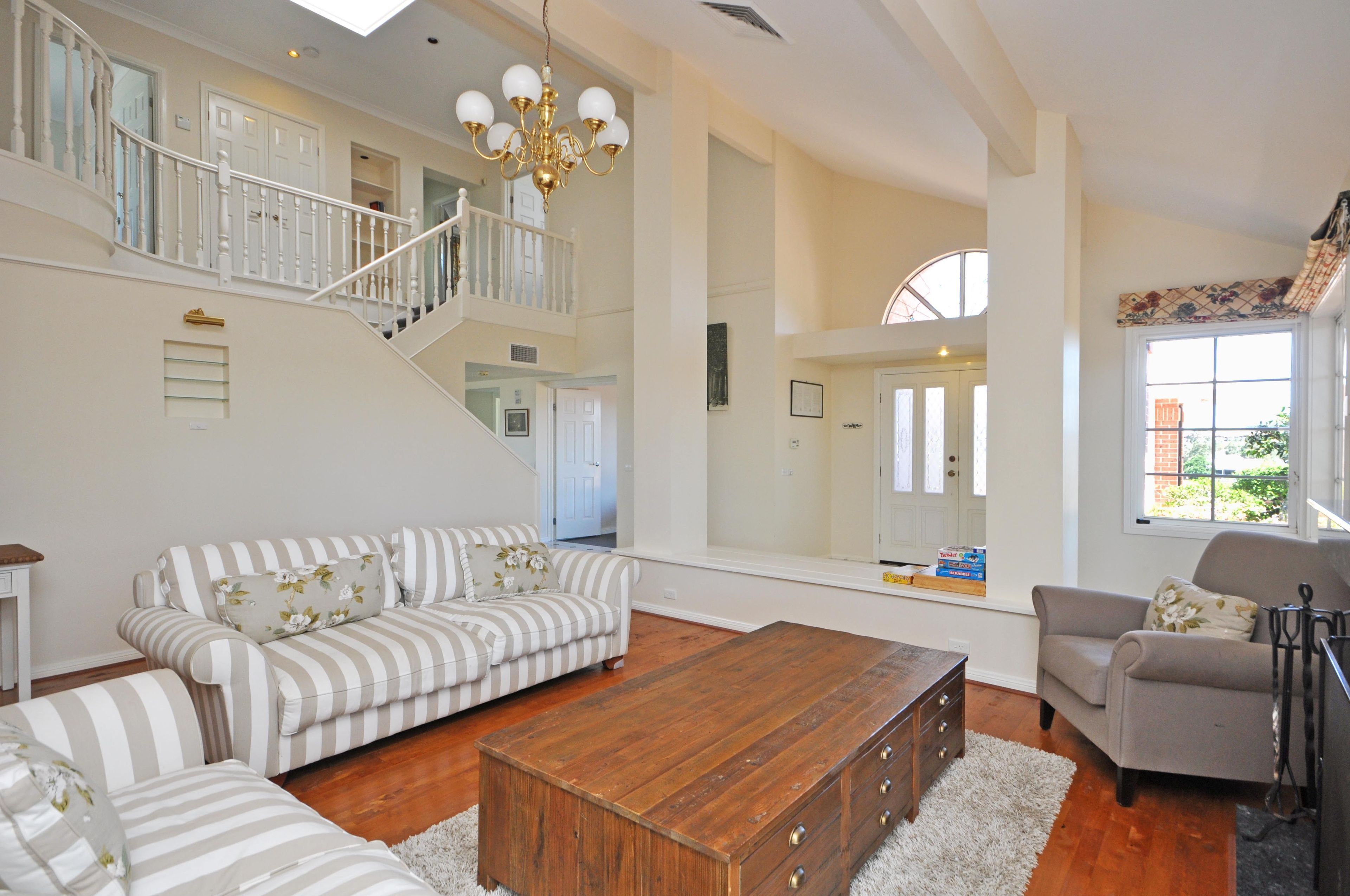 A spacious living room with a staircase, a wooden coffee table, and striped sofas.