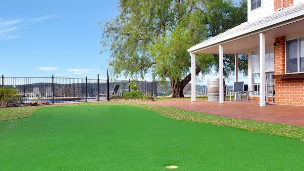 A green artificial turf golf course with a white building and a fence in the background. - Beggars Bridge Vineyard Homestead Pool Tennis (Rothbury)