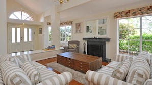 A spacious living room with a fireplace, striped sofas, a wooden coffee table, and a chandelier. - Beggars Bridge Vineyard Homestead Pool Tennis (Rothbury)
