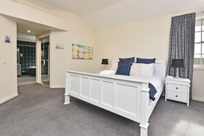 A bedroom with a white bed, a nightstand, a lamp, a painting, and a view of the outdoors.