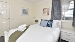 A hotel room with a bed, a nightstand, a window with curtains, and two framed artworks on the wall. - Beggars Bridge Vineyard Homestead Pool Tennis (Rothbury)