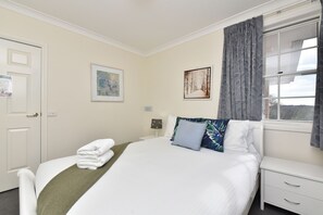 Habitació d'hotel amb un llit, una tauleta de nit, una finestra amb cortines i dues obres d'art enmarcades a la paret.