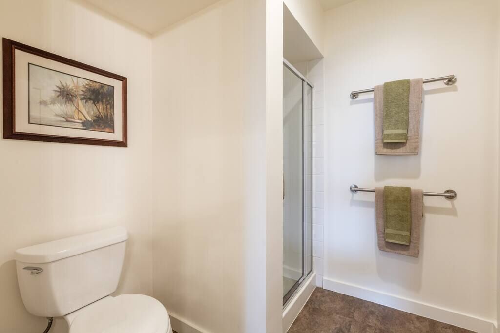 A bathroom with a toilet, a glass shower enclosure, and two towels on a rack.