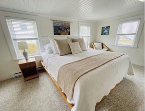 A bedroom with a bed, nightstand, and two windows.