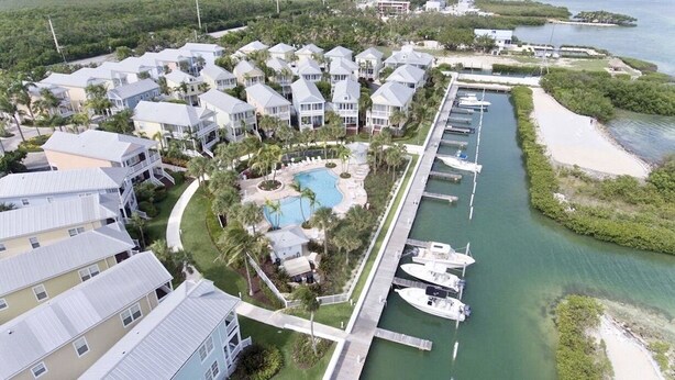 An aerial view of a coastal residential area with multiple houses, a swimming pool, and a marina with boats. - OCEANSIDE  ANGLERS REEF HOME- Gated community- Pool, Dock, Private Beach (Islamorada)