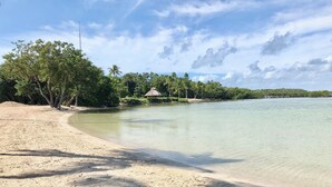 A beach with clear water, a sandy shore, and a thatched-roof hut surrounded by trees. - OCEANSIDE  ANGLERS REEF HOME- Gated community- Pool, Dock, Private Beach (Islamorada)