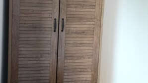 Un armario de madera con dos puertas y tiradores, situado frente a una pared lisa con suelo de madera.