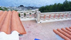 Una terraza con techo de tejas que da a un litoral rocoso y zonas verdes.