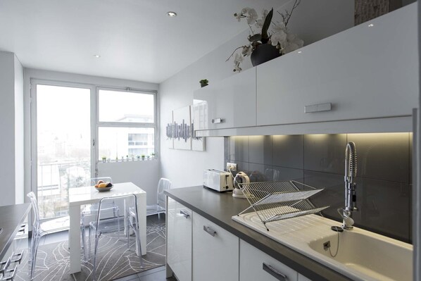 A modern kitchen with a large window, a dining area with a table and chairs, and a sink with a faucet. - Steps from the Eiffel Tower, by Veeve (Paris)