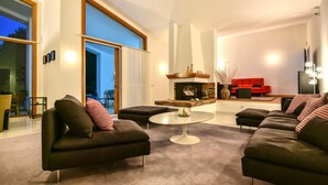Ein modernes Wohnzimmer mit Kamin, schwarzen Sofas, einem runden Couchtisch und einem roten Sofa im Hintergrund.