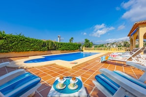 A pool area with lounge chairs and a table with two cups and a muffin.
