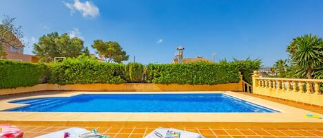 A swimming pool with lounge chairs and towels, surrounded by greenery and a clear sky.
