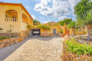 A courtyard with a stone pathway leading to a building with arches and a tiled roof.