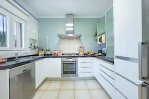 Una cucina moderna con mobili bianchi, elettrodomestici in acciaio inossidabile e pavimento piastrellato.